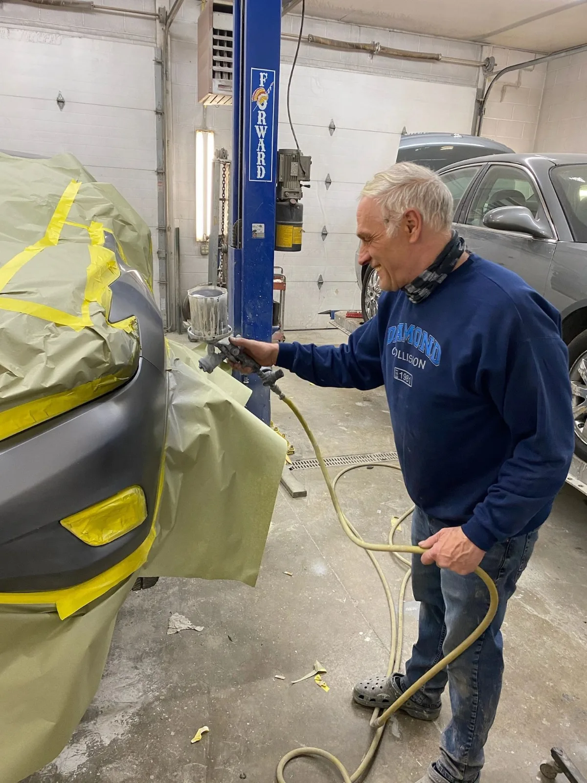 Chuck Mastrodonato spraying paint on a masked-off car in the shop