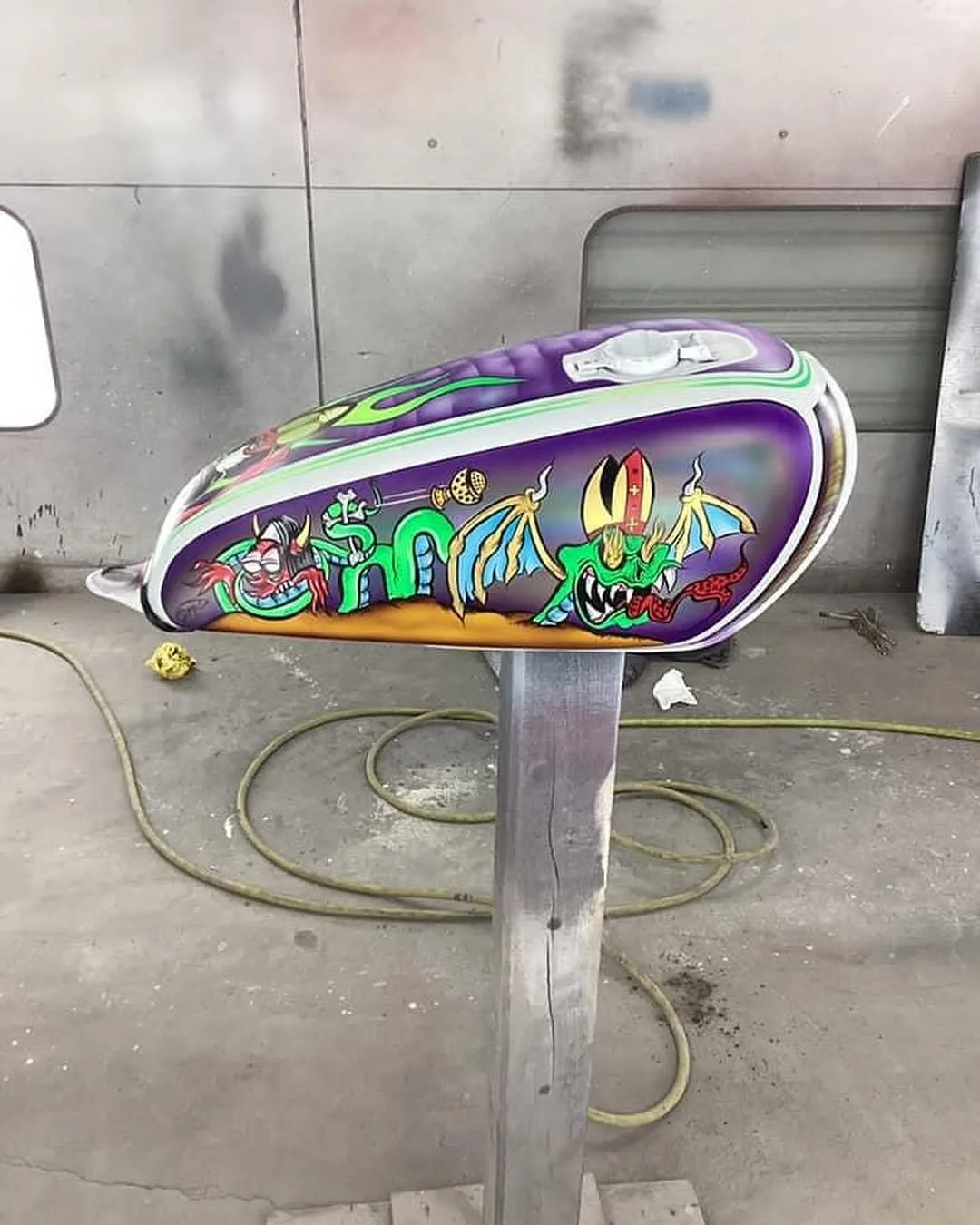 A motorcycle gas tank custom-painted in purple with cartoon monsters