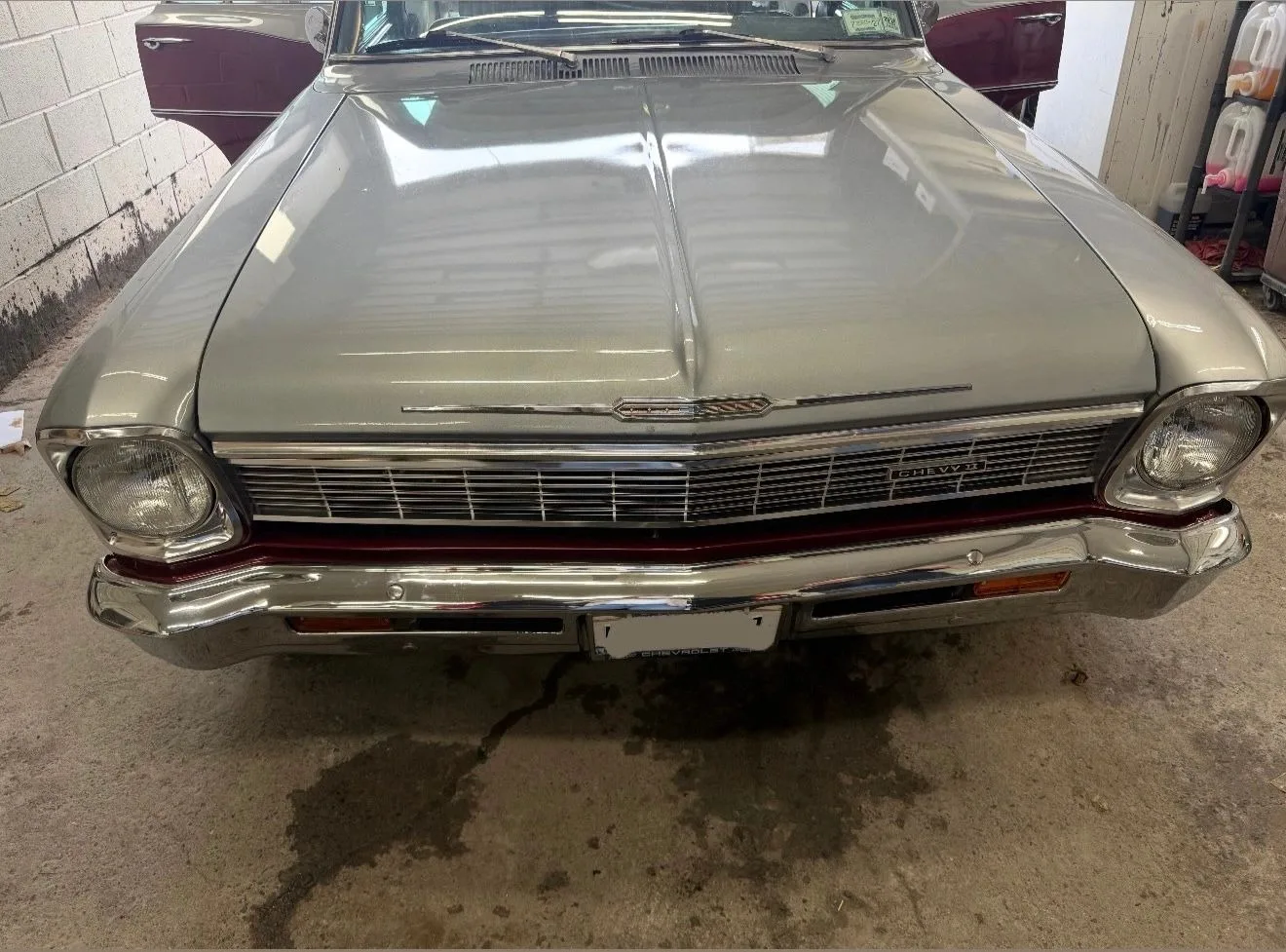 The front of a restored silver Chevy II with its chrome grille and bumper