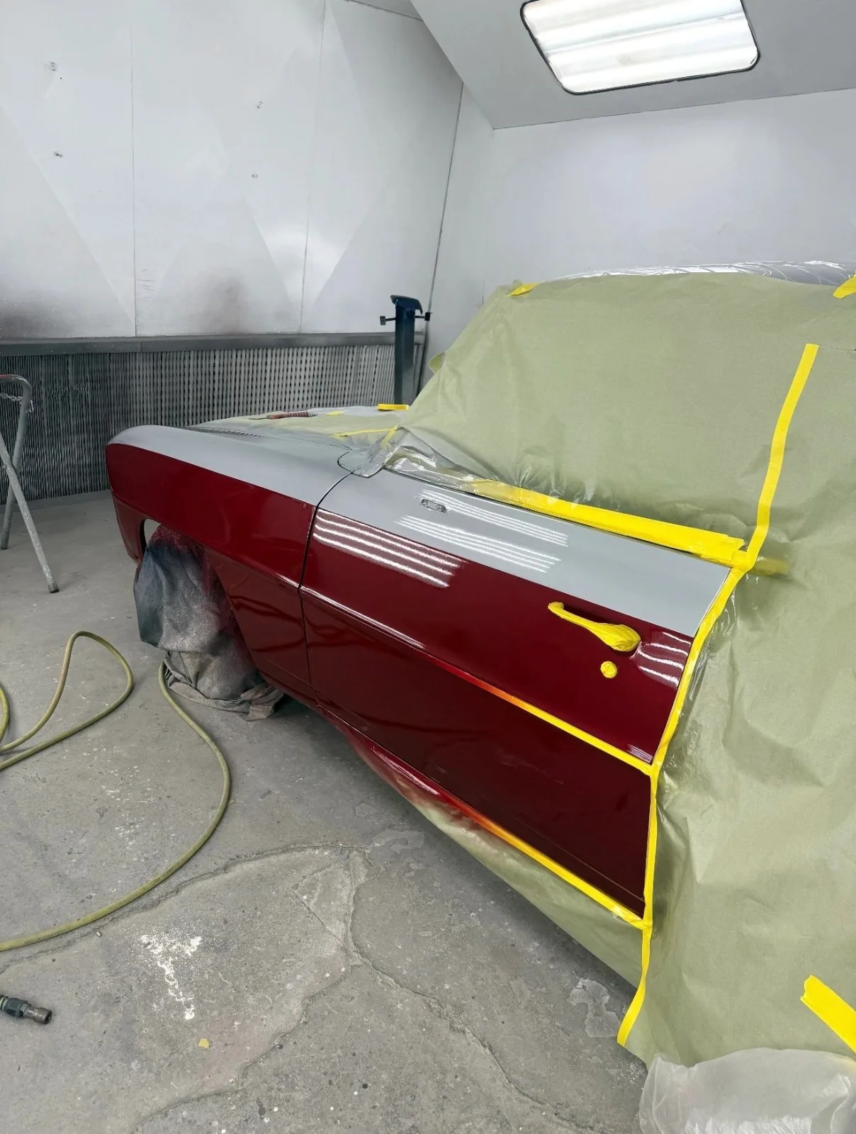 A burgundy door panel masked off with yellow tape in the paint booth