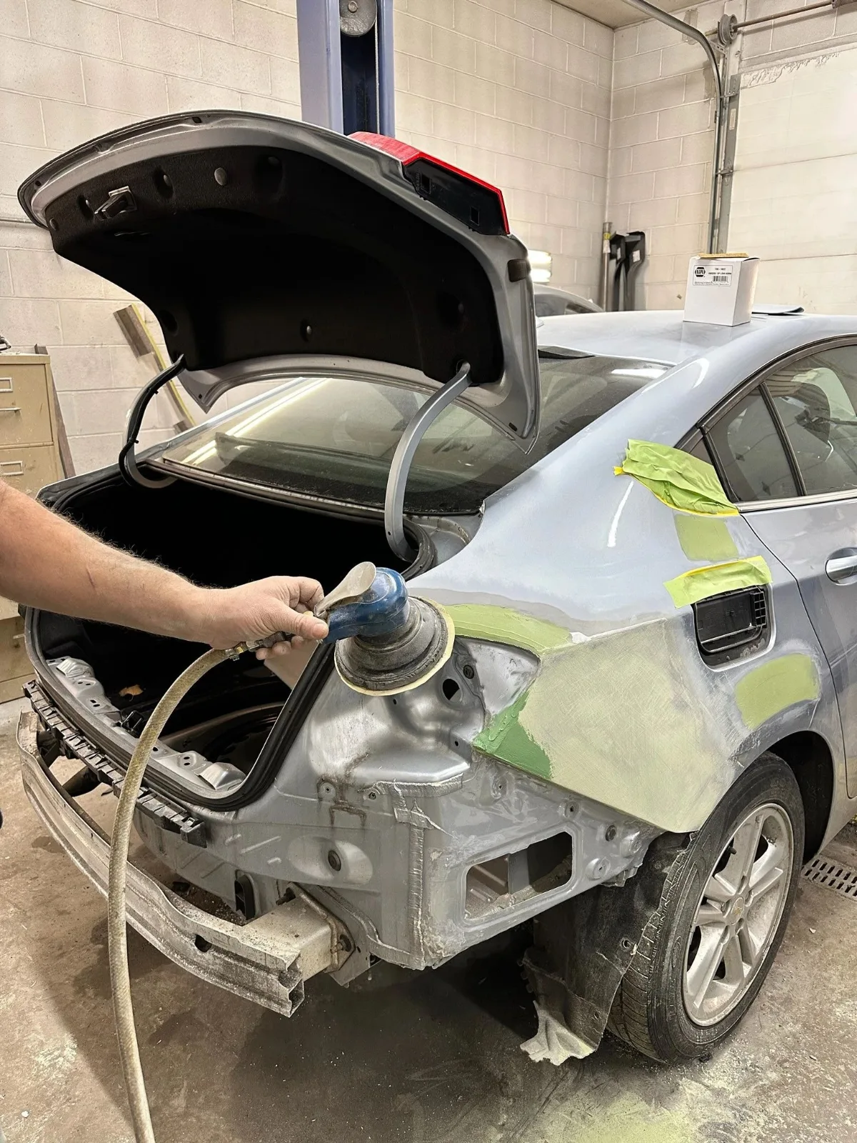 A rear quarter panel being sanded smooth, with the trunk lid raised